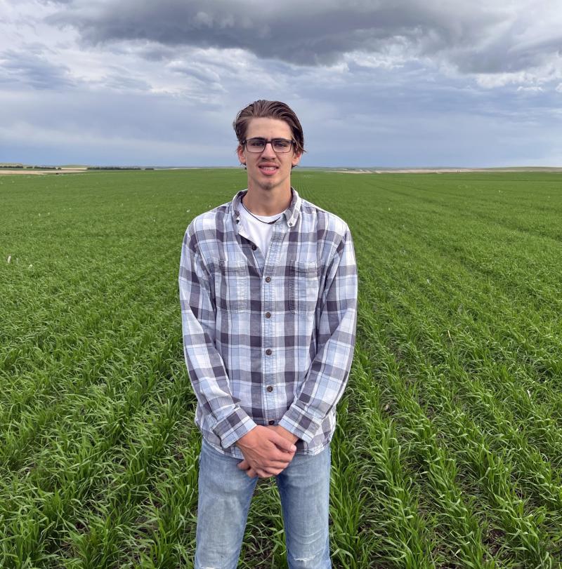 A man smiles for the camera standing outside in a field of row crops