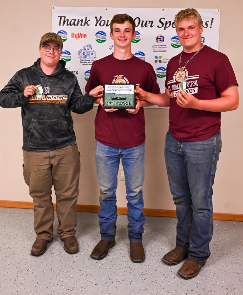 Three teenage boys hold their medals and a plaque
