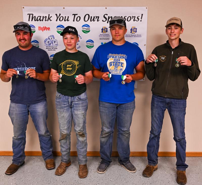 Four boys stand in a row holding up their medals