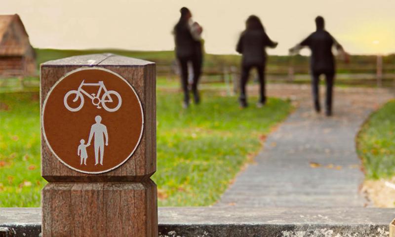Sign posted alongside a rural walking and biking path with a family walking in the distance.