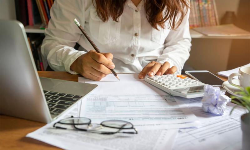 Young woman sitting at a laptop computer. She is reviewing a collection of bills.