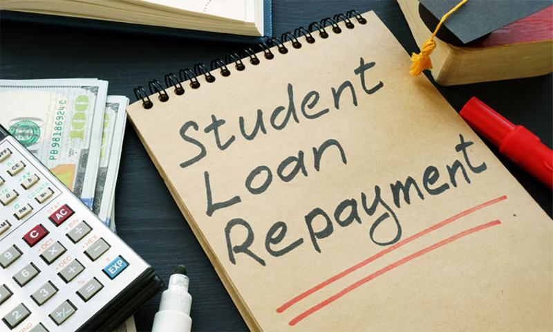 Calculator, cash, and notebook with the words “Student Loan Repayment” written on it.