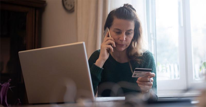 Woman at a laptop holding a credit card while talking to a customer service agent.