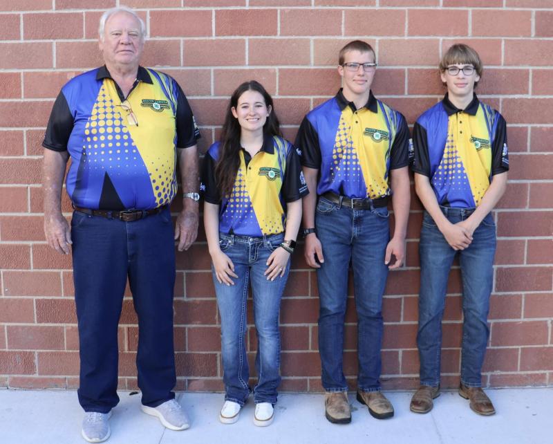 An adult male and three youth stand in front of a brick wall and smile for the camera