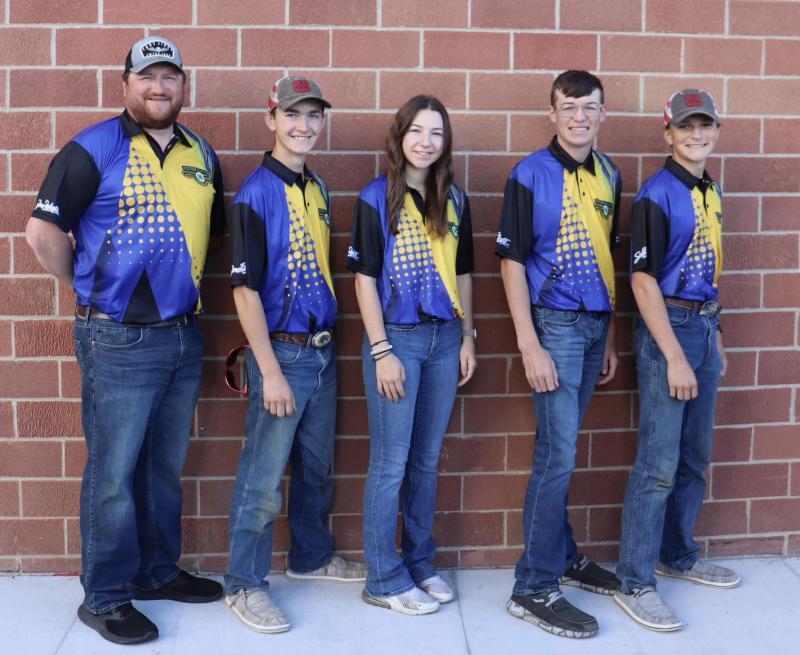 An adult male and four youth stand in front of a brick wall and smile for the camera
