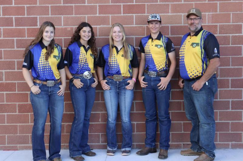 Four youth and their coach stand in front of a brick wall and smile for the camera