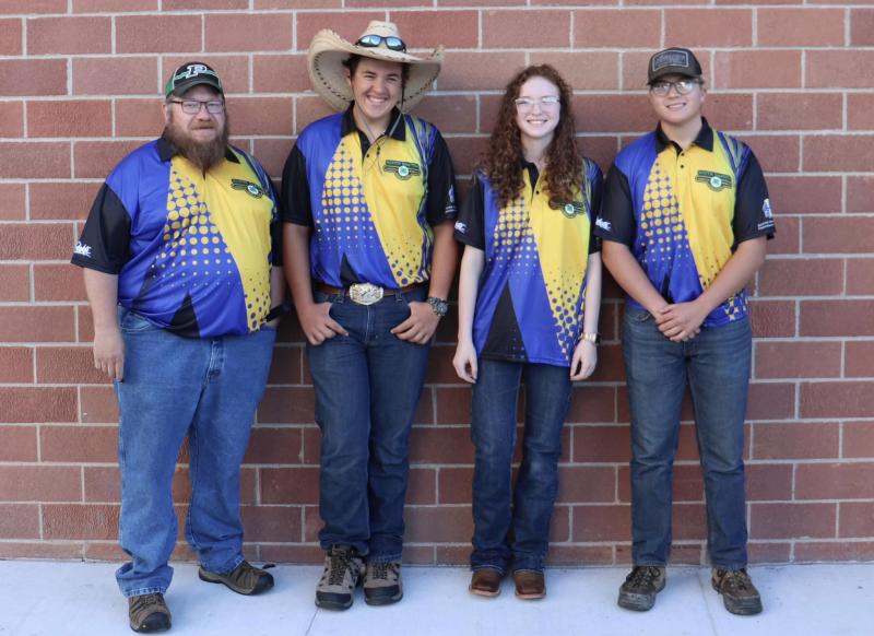 Three youth and their coach stand in front of a brick wall and smile for the camera