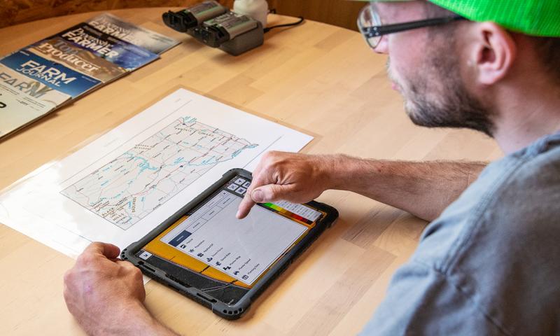 Young farmer at a table using smart device to review data and plan a customized seed application.