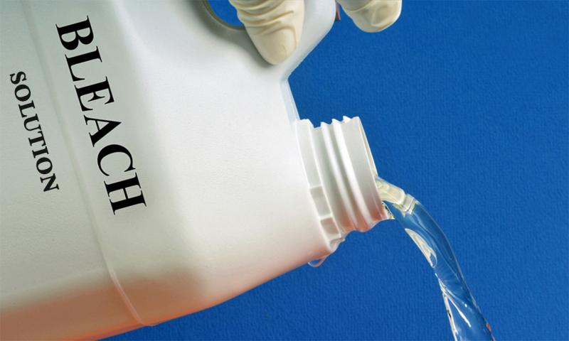 Hand pouring out a bleach solution from a plastic container.