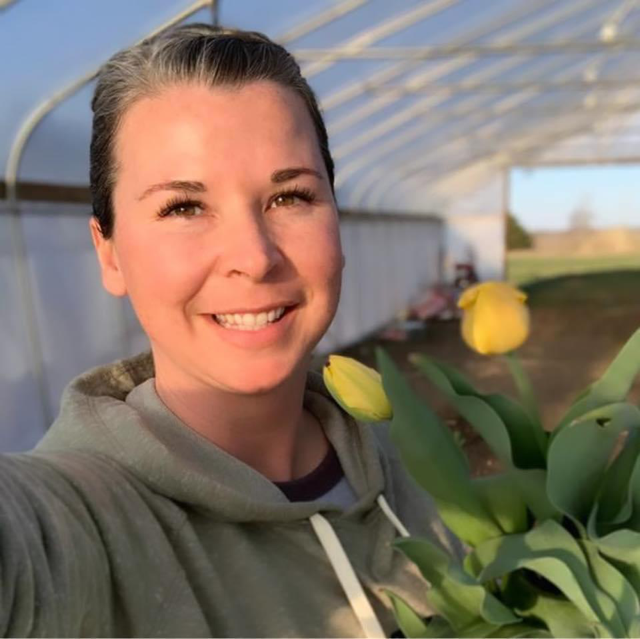 A woman inside a high tunnel smiles for a selfie