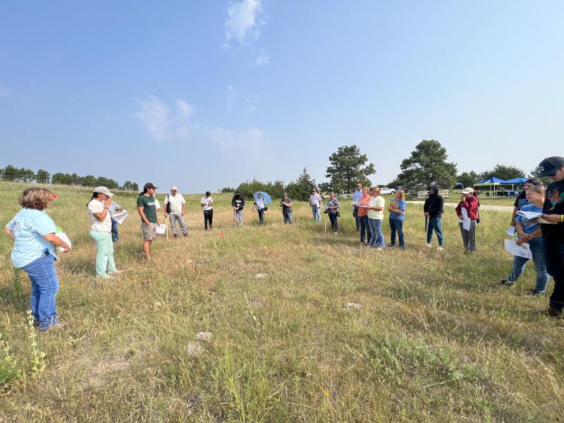 A group of people stands in a circle in a pasture