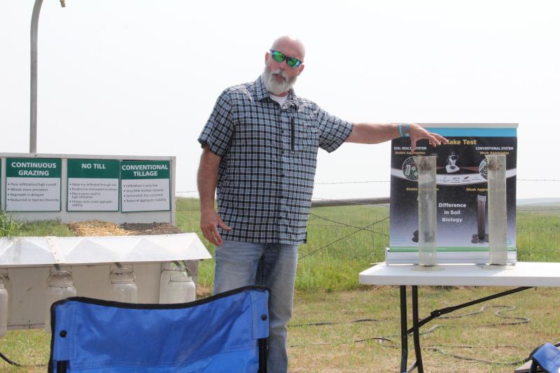 A man motions to rainfall simulator while speaking to an audience