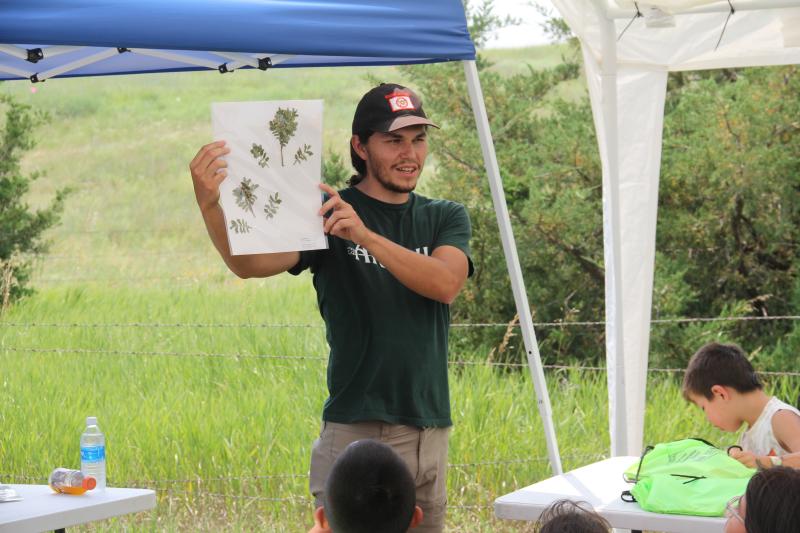 A man holds up a piece of paper with plants displayed to an audience of youth