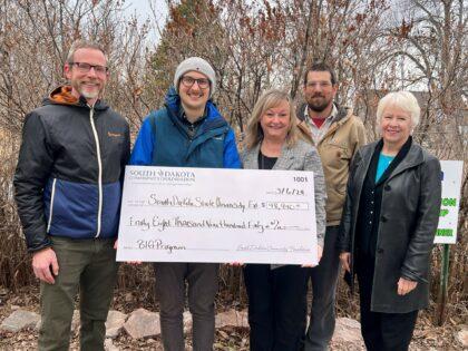 Five people stand with a giant check for $48,940