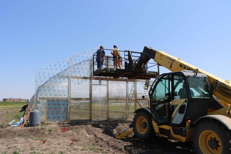 Two people stand in a scaffolding to work on high tunnel being constructed
