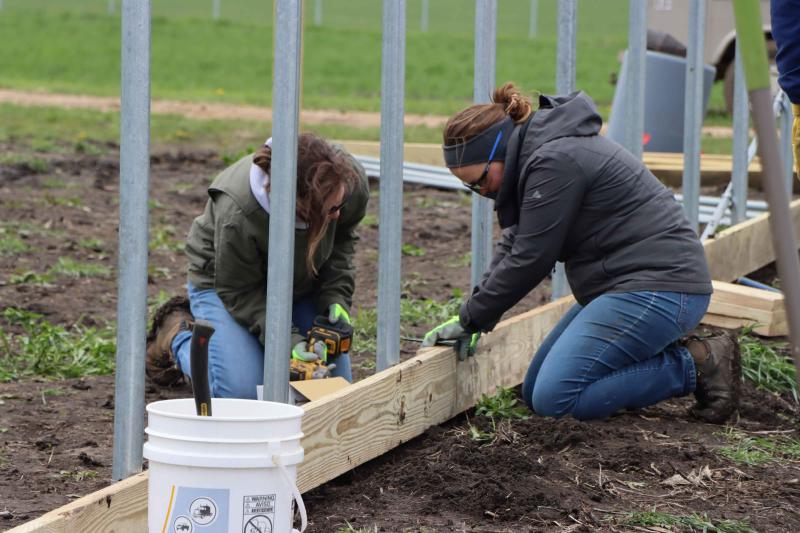 Two women work on the base of a high tunnel