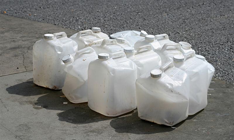 Several damaged plastic pesticide containers grouped together on a driveway.