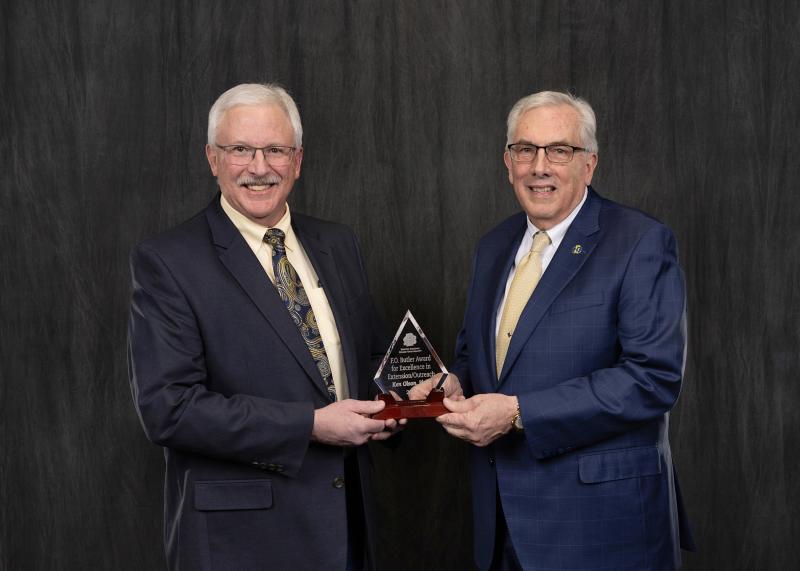 Two men smile for the camera holding a glass award