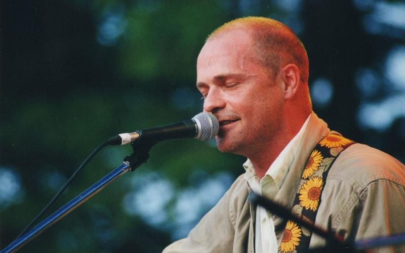 Gord Downie leaning into a microphone on an outdoor stage.