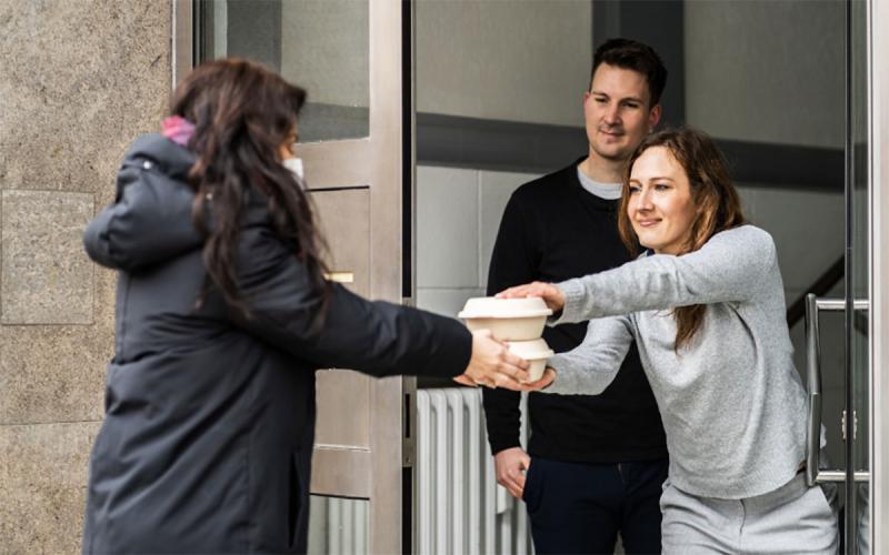 A young woman in winter clothing delivering a meal to her neighbors’ apartment.