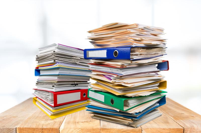 A stack of binders and file folders on a wood table.