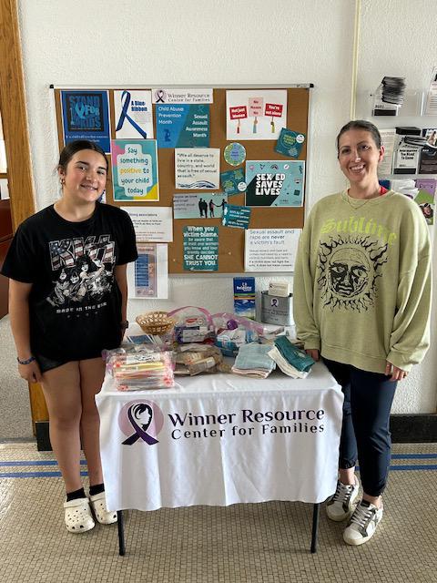 A girl and a woman stand on either side of a table stacked with donated hygiene items