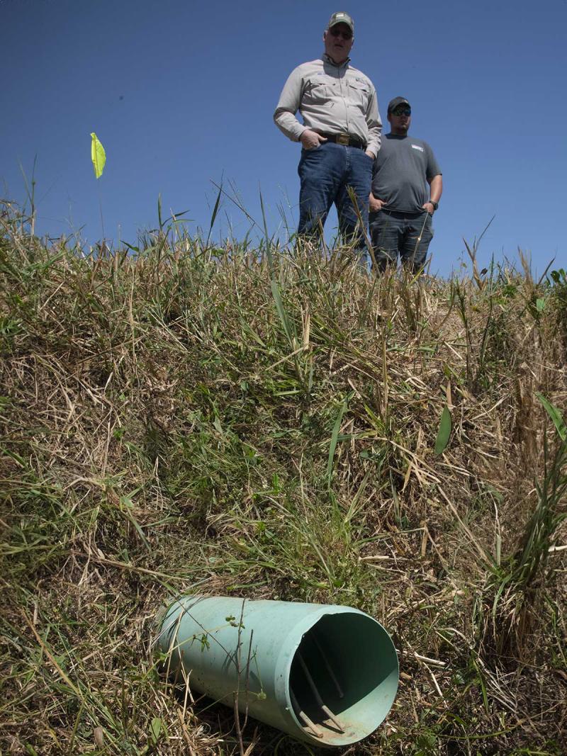 Two producers inspect a subsurface drainage pipe on the edge of a field.