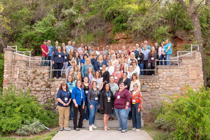 A large group of people stands on a stone staircase to smile for a photo