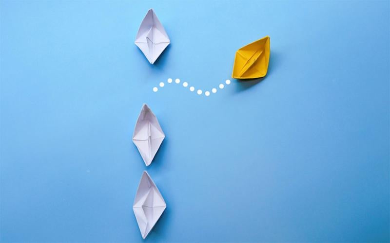 A line of paper boats, with a single yellow boat veering off on it’s own path, symbolizing laissez faire leadership style.