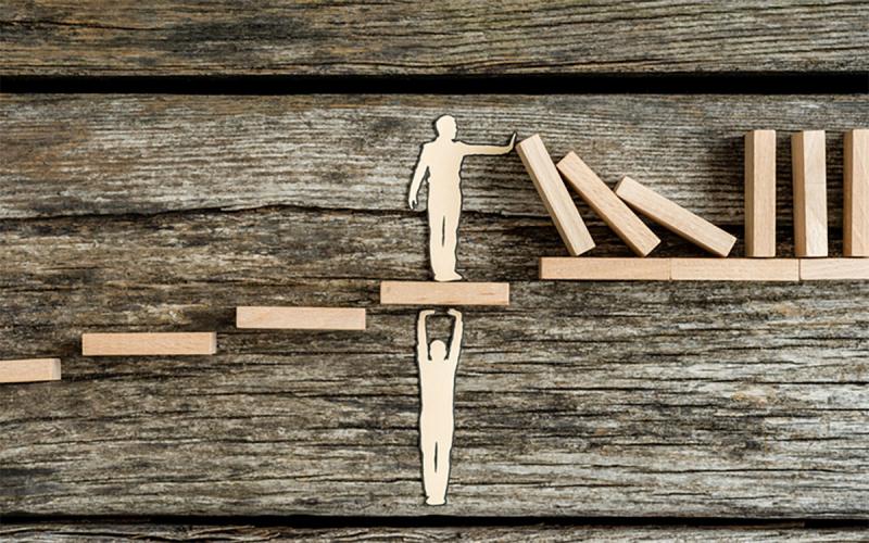 A wooden figure standing on a platform being held up by another wooden figure, symbolizing servant leadership style.