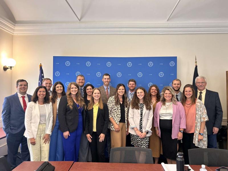 A group of people stands in front of a blue backdrop