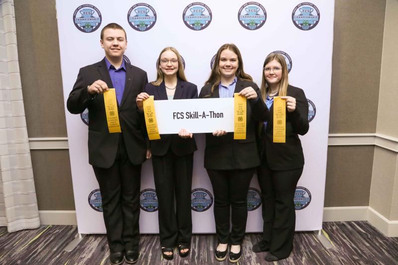 Four youth stand with yellow ribbons and a sign that says FCS skill-a-thon