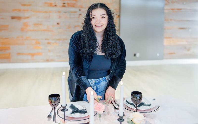 Brianna Munoz arranging place settings and flowers in an event hall.