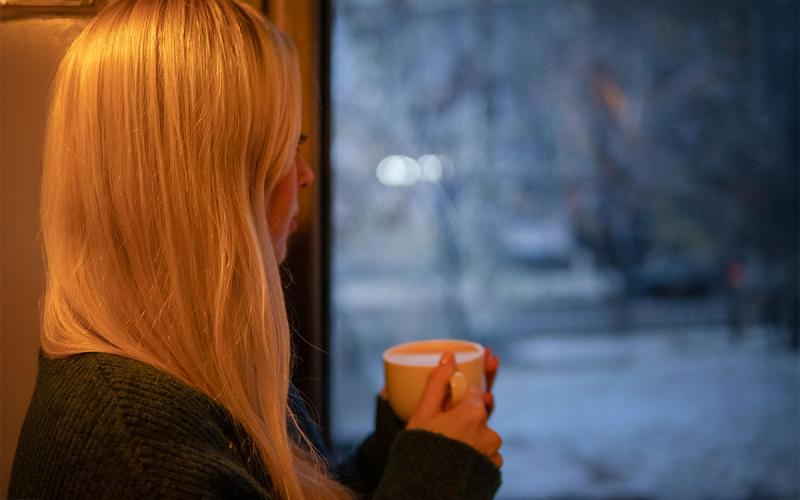Woman in black knit Long-sleeved shirt holding white ceramic mug.