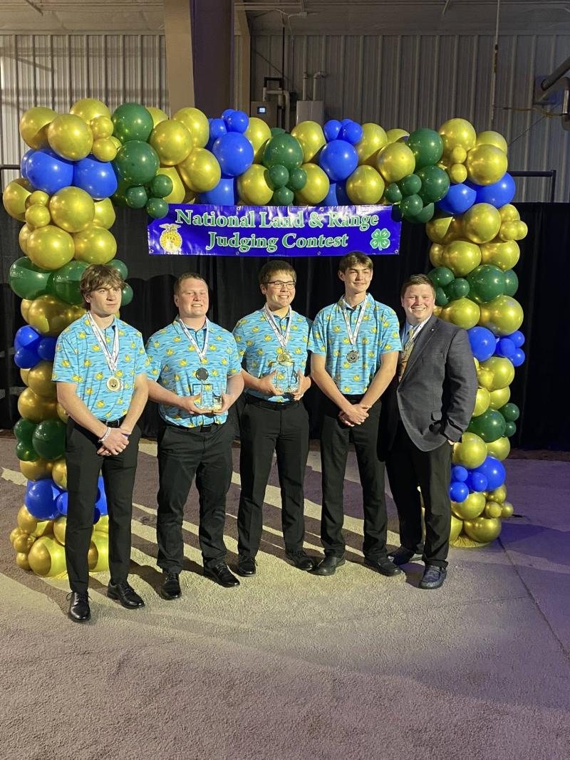 Four teenage boys and a man stand under a blue and green balloon arch with a banner that reads &quot;National Land and Range Judging Contest&quot;