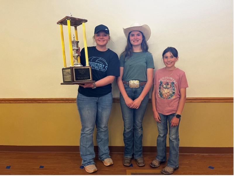 A girl holds a large trophy and two others smile with her for the camera