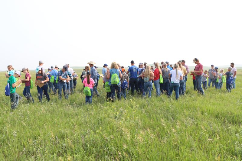 A group of youth and adults stand in a grassy pasture