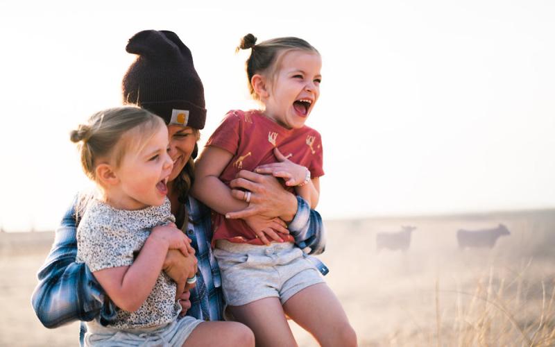 Mother holding two daughters outdoors in the countryside.