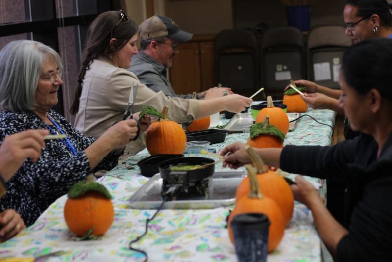 People sit at a long white table painting pumpkins