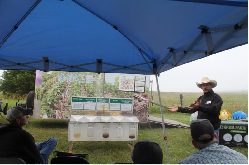 A man stands beside a rainfall simulator inside a tent
