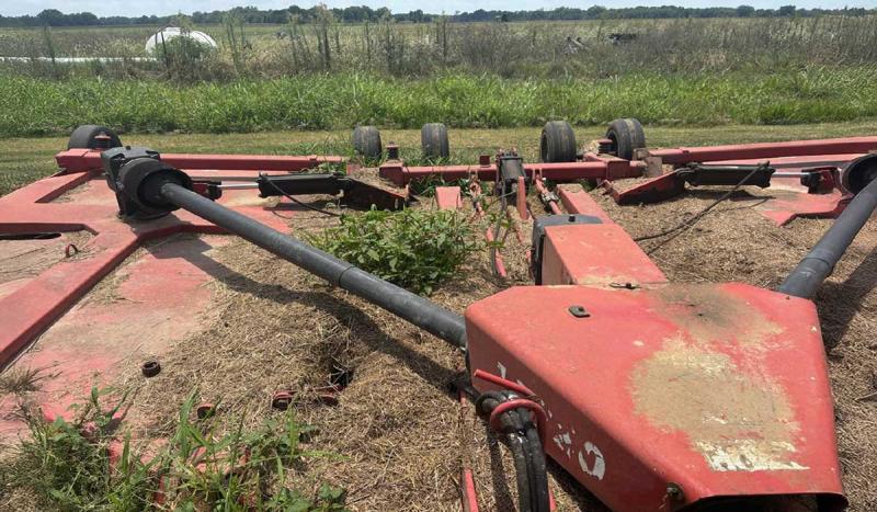 A red mower that has brown residue on top with green weeds growing from the residue.