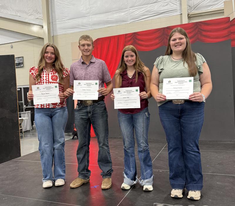 Four youth smile with certificates