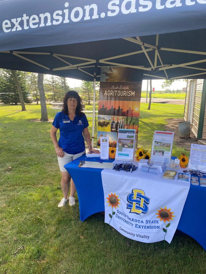 A woman in a blue shirt stands next to an agritourism display