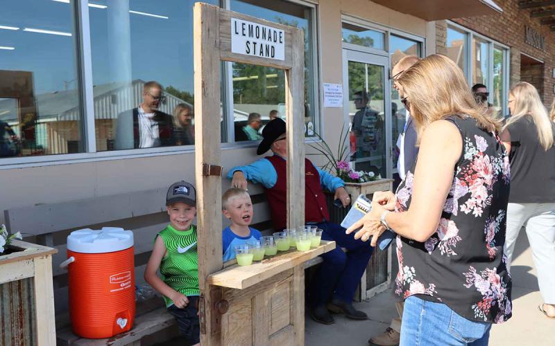 Woman buying lemonade from two children outside of a grocery store.