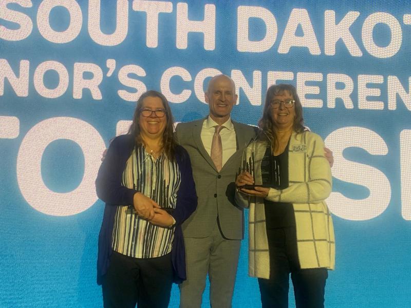 Two women and a man smile while holding their agritourism awards