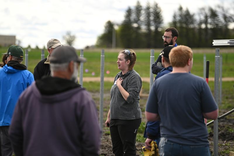 A woman with brown hair in a braid wearing a grey T-Shirt with an SDSU Extension logo stands in the middle of a group of people at a construction site