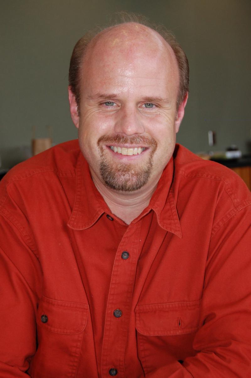 A mean in a red button-up shirt smiles for the camera