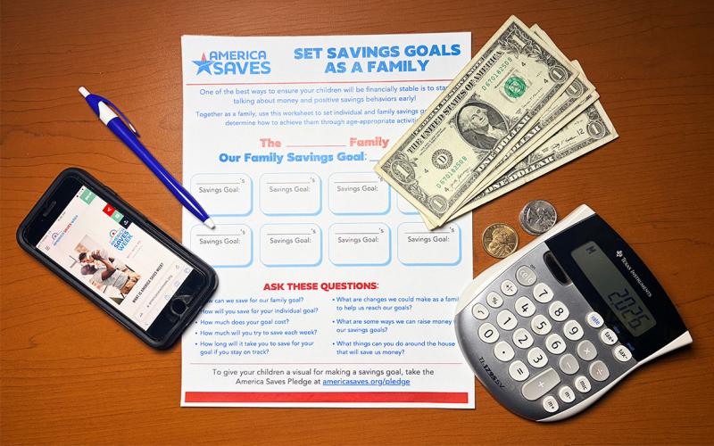 America Saves Week pledge form on a desk along with cash, a calculator, and smartphone.