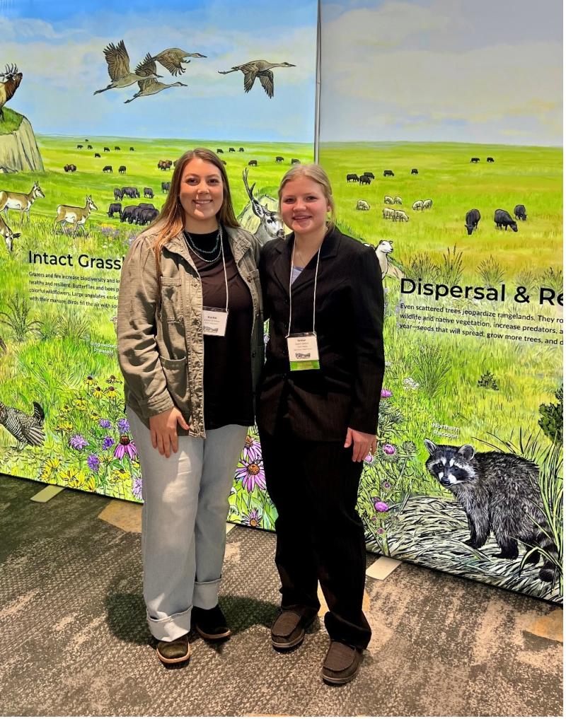 Two females smile for the camera in front of a painted range backdrop