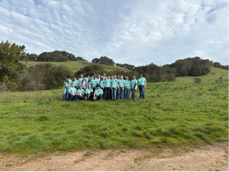A group of people in an open pasture wearing light blue shirts smile for the camera